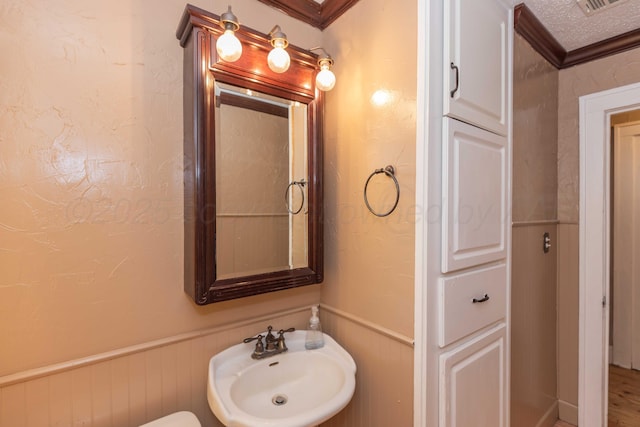 half bathroom featuring a wainscoted wall, crown molding, a textured wall, a sink, and a textured ceiling