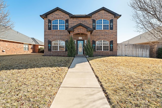 traditional-style home with brick siding, fence, and a front lawn