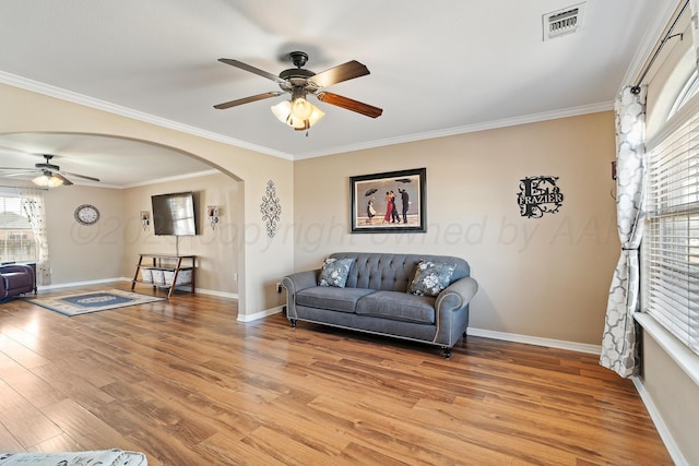 living area with arched walkways, light wood finished floors, visible vents, ornamental molding, and baseboards