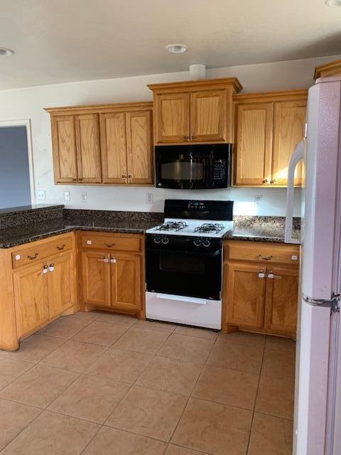 kitchen with dark stone counters, white appliances, and light tile patterned floors