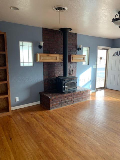 unfurnished living room featuring hardwood / wood-style floors, a wood stove, and a textured ceiling