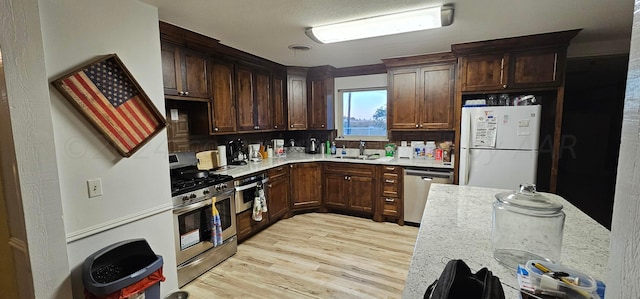 kitchen with light stone counters, appliances with stainless steel finishes, sink, decorative backsplash, and light hardwood / wood-style flooring