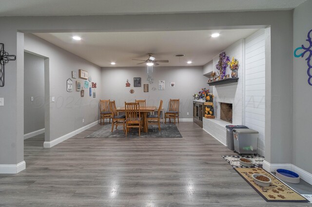 dining area featuring hardwood / wood-style flooring, ceiling fan, and a brick fireplace