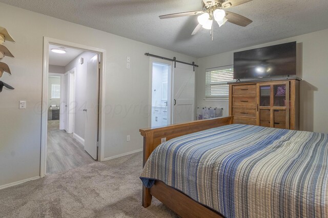 carpeted bedroom featuring a textured ceiling, a barn door, ceiling fan, and ensuite bathroom