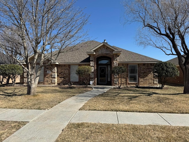 ranch-style house with brick siding, a front yard, and a shingled roof