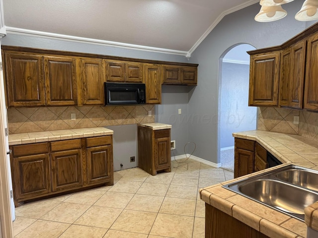 kitchen with tile counters, black microwave, crown molding, and vaulted ceiling