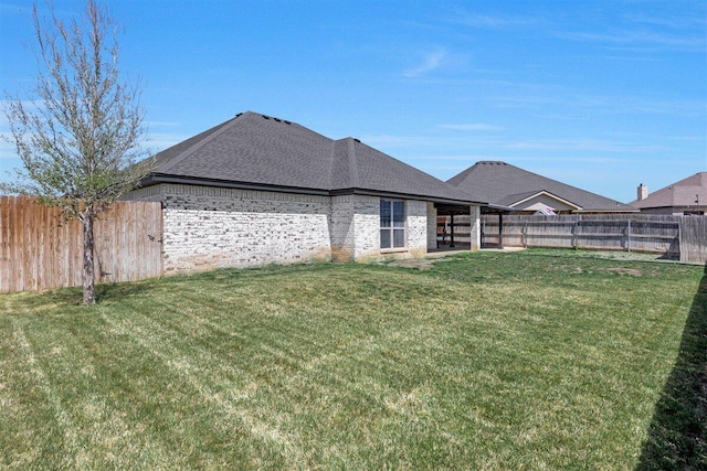 exterior space with a shingled roof, brick siding, a lawn, and a fenced backyard