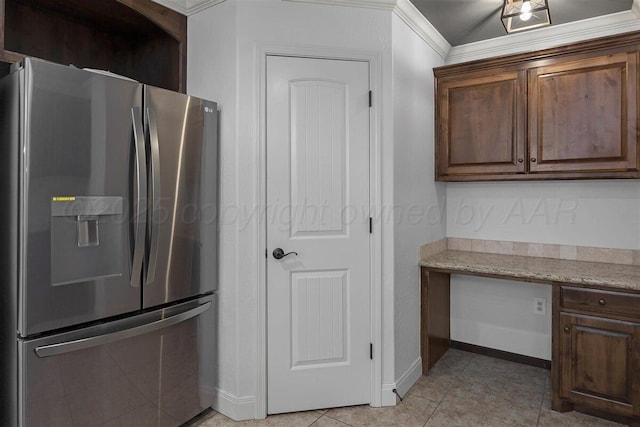 kitchen with baseboards, light tile patterned floors, stainless steel fridge, crown molding, and built in desk