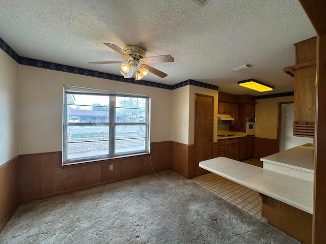 interior space with a wainscoted wall, a ceiling fan, and a textured ceiling