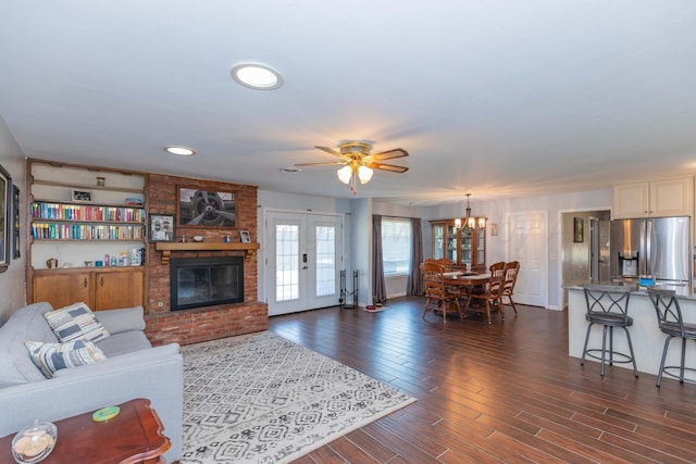living room featuring a brick fireplace, dark wood-style floors, and ceiling fan with notable chandelier