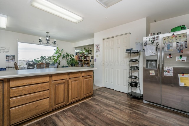 kitchen with dark wood-style flooring, a notable chandelier, light countertops, brown cabinetry, and stainless steel fridge