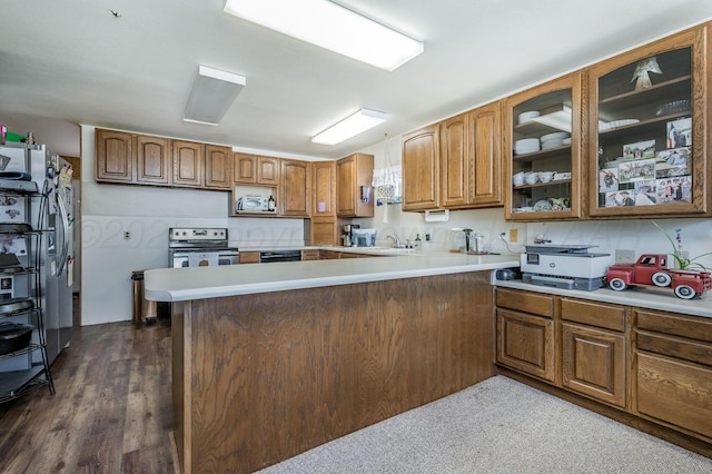 kitchen with stainless steel appliances, light countertops, brown cabinetry, glass insert cabinets, and a peninsula