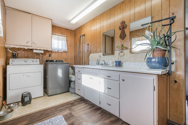 washroom with cabinet space, a sink, wood walls, separate washer and dryer, and wood finished floors