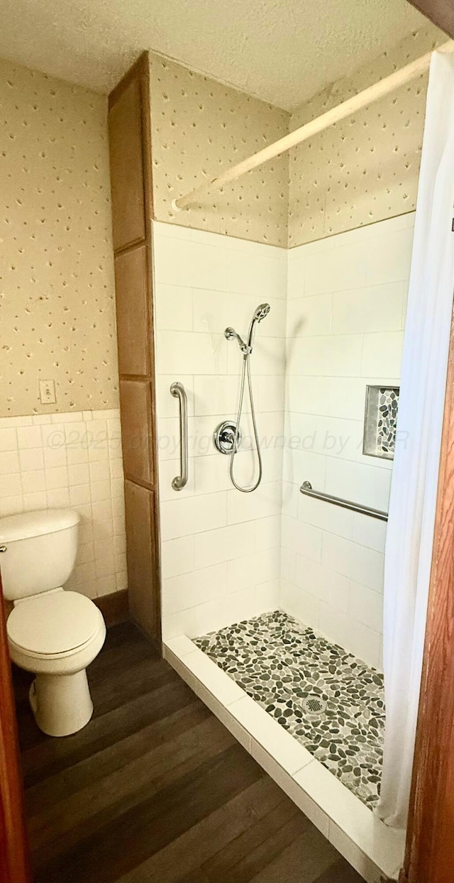 full bath featuring wainscoting, a shower stall, wood finished floors, toilet, and wallpapered walls