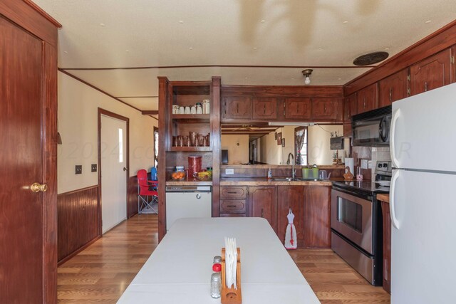 kitchen with sink, white appliances, wooden walls, and light hardwood / wood-style flooring