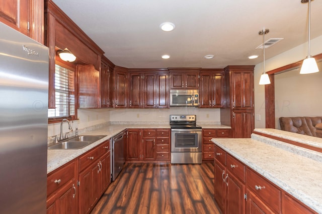 kitchen featuring stainless steel appliances, sink, light stone countertops, dark hardwood / wood-style floors, and hanging light fixtures