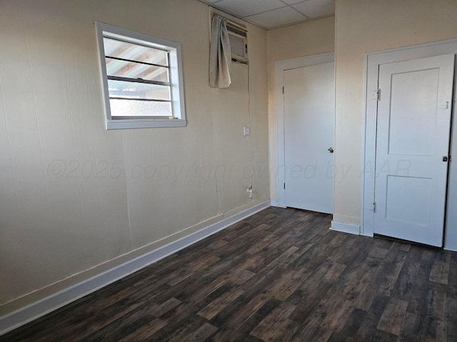 unfurnished bedroom with dark wood-type flooring, a wall mounted AC, and a drop ceiling