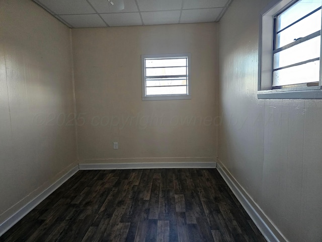 empty room featuring plenty of natural light, dark hardwood / wood-style floors, and a drop ceiling