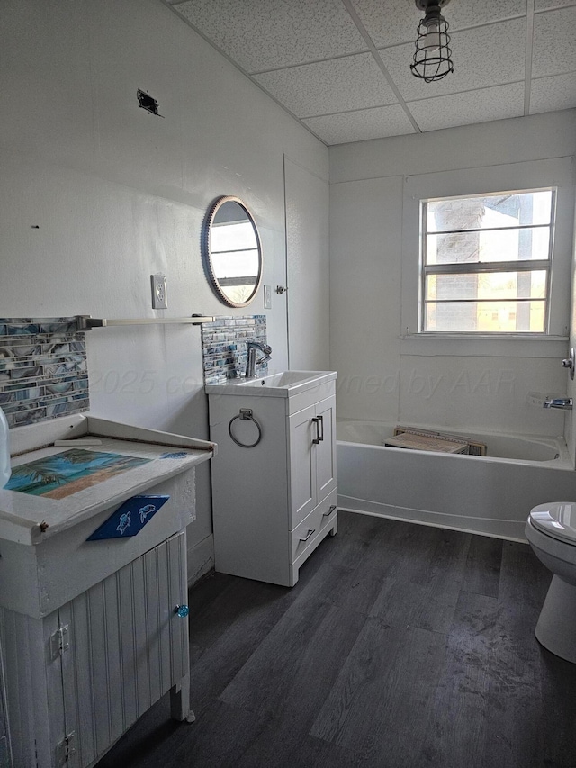 bathroom featuring toilet, a paneled ceiling, vanity, hardwood / wood-style floors, and a washtub
