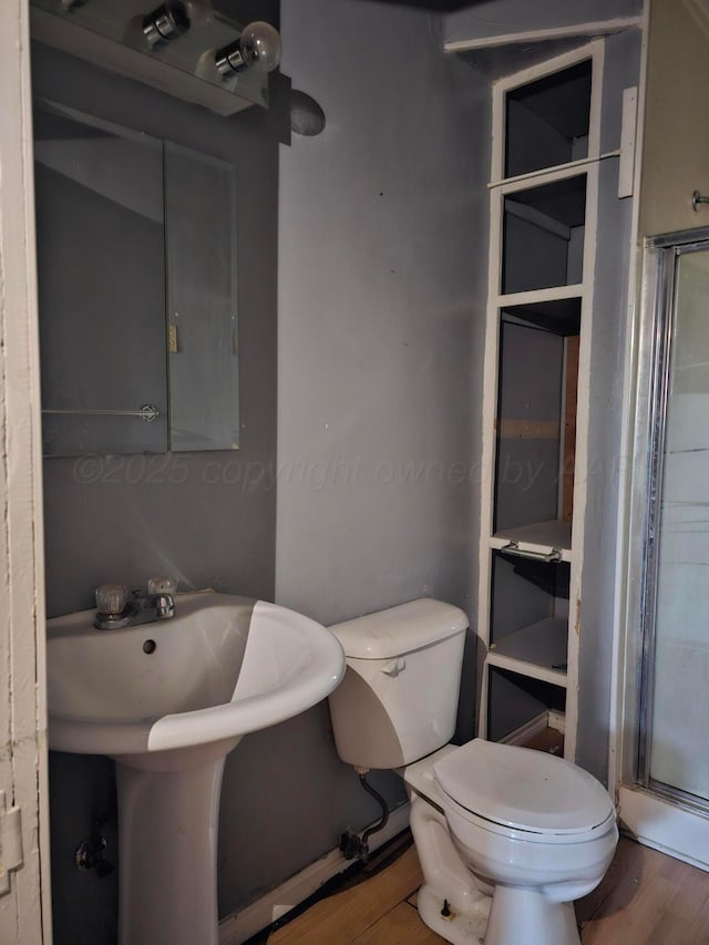 bathroom with wood-type flooring, toilet, and a shower with shower door