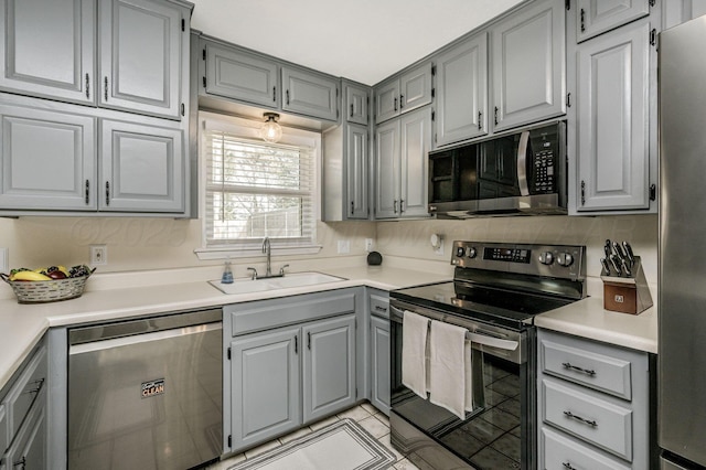 kitchen with gray cabinetry, sink, light tile patterned flooring, and stainless steel appliances