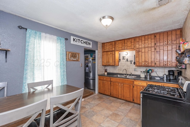 210 Oak Ave, Dumas, TX 79029 - kitchen featuring black range with gas cooktop, dark countertops, brown cabinets, stainless steel fridge, and a textured ceiling