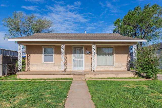 bungalow-style home with fence, stucco siding, covered porch, stone siding, and a front yard