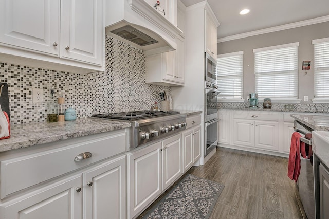 kitchen featuring crown molding, appliances with stainless steel finishes, wood-type flooring, white cabinets, and custom exhaust hood