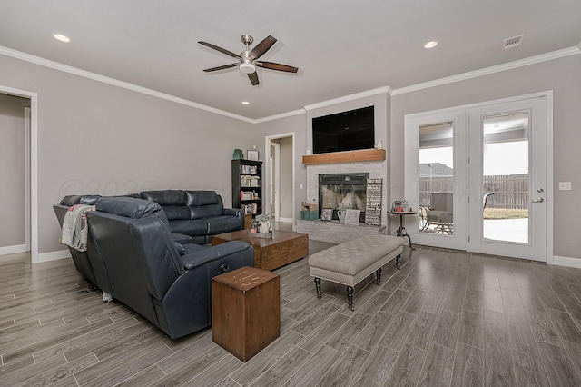 living room featuring crown molding, a stone fireplace, ceiling fan, and light wood-type flooring