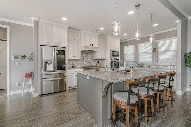 kitchen featuring appliances with stainless steel finishes, white cabinets, a large island, light stone counters, and crown molding