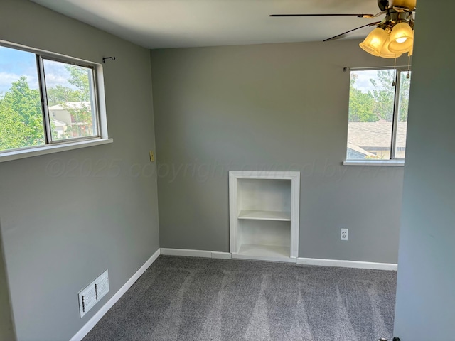 spare room with a ceiling fan, visible vents, built in shelves, baseboards, and carpet flooring