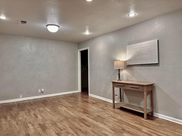 unfurnished room with light wood-type flooring and a textured ceiling