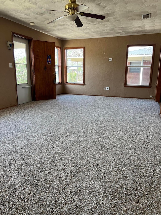 unfurnished room featuring a ceiling fan, a wealth of natural light, a textured ceiling, and visible vents