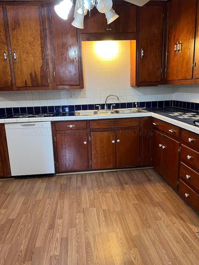 kitchen featuring backsplash, white dishwasher, light wood-style flooring, and a sink