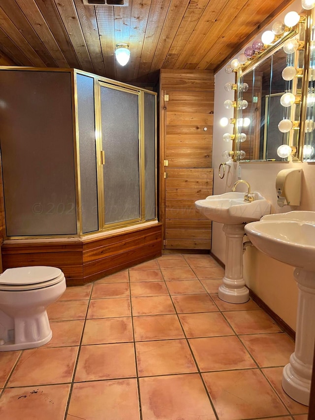 bathroom featuring wood walls, wood ceiling, tile patterned flooring, toilet, and combined bath / shower with glass door