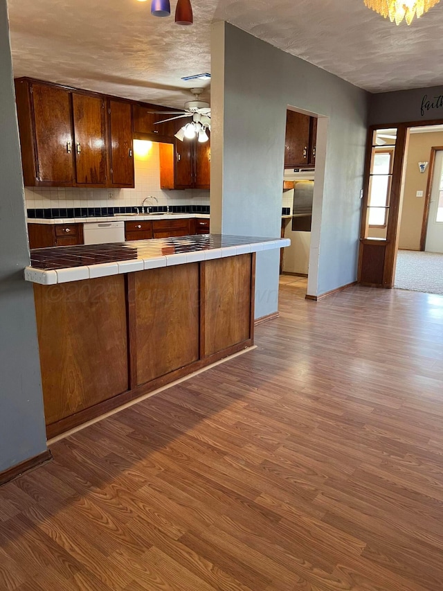 kitchen featuring a sink, tile counters, tasteful backsplash, ceiling fan, and dark wood-style flooring