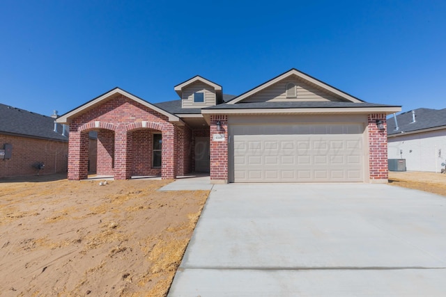 single story home with a garage, concrete driveway, brick siding, and central AC