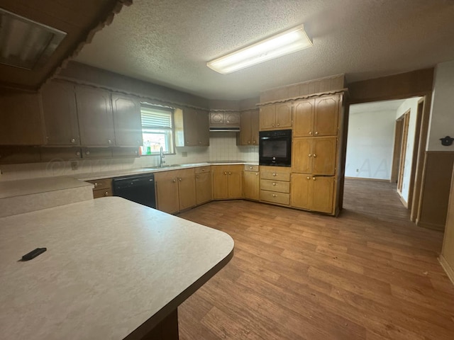 kitchen featuring a textured ceiling, a sink, light countertops, black appliances, and light wood finished floors