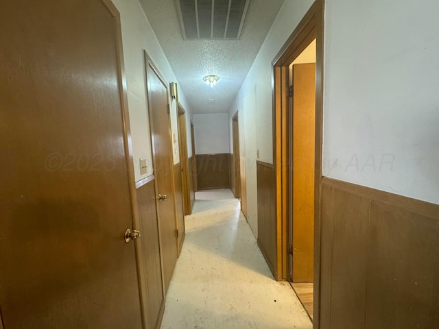 corridor with concrete flooring, a textured ceiling, wainscoting, and visible vents