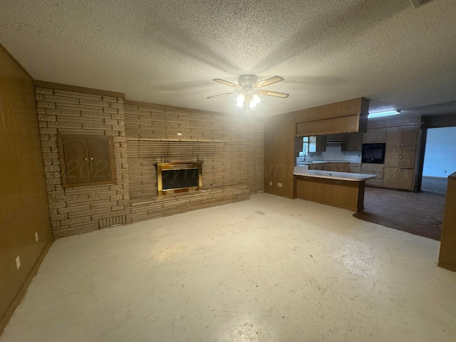 unfurnished living room with a textured ceiling, ceiling fan, a fireplace, and unfinished concrete floors