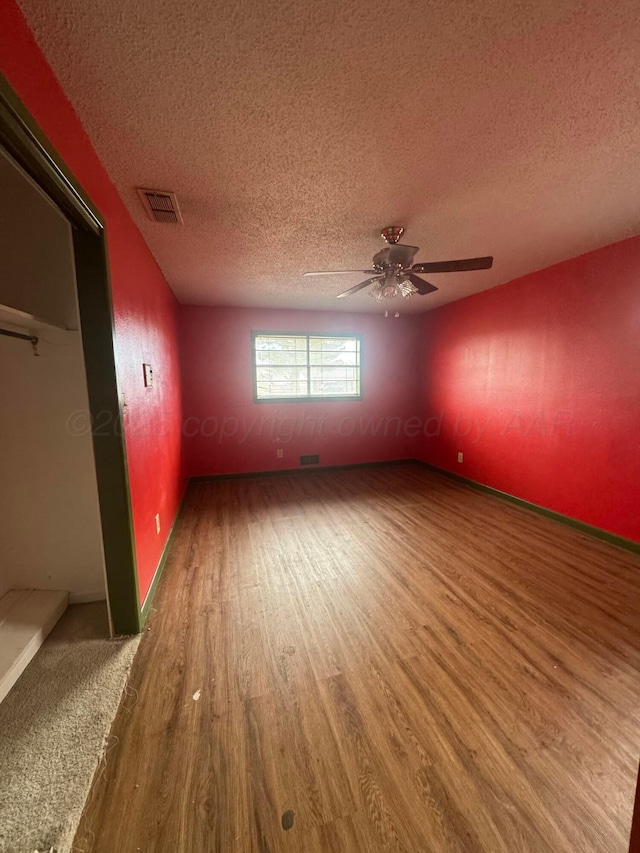 unfurnished room featuring visible vents, ceiling fan, a textured ceiling, and wood finished floors