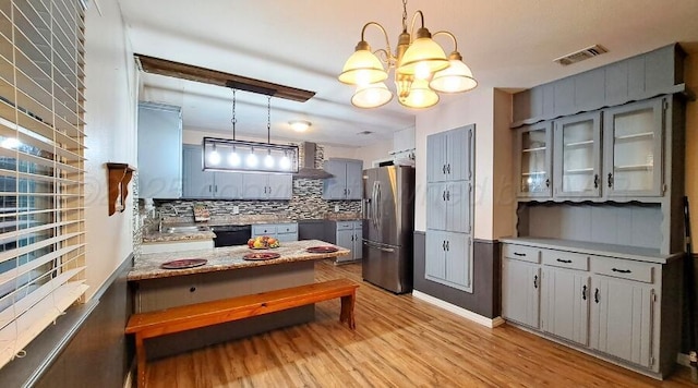 kitchen with an inviting chandelier, stainless steel fridge, backsplash, decorative light fixtures, and light wood-type flooring