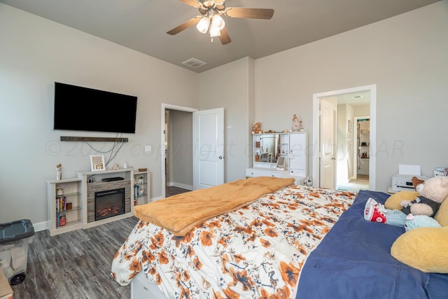 bedroom featuring a stone fireplace, hardwood / wood-style flooring, and ceiling fan