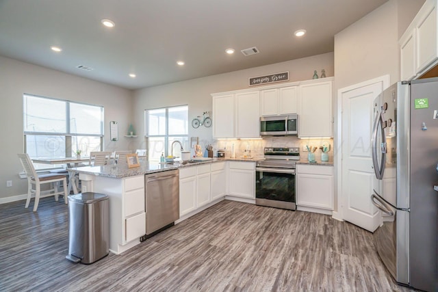 kitchen featuring stainless steel appliances, light stone counters, kitchen peninsula, white cabinetry, and light hardwood / wood-style flooring