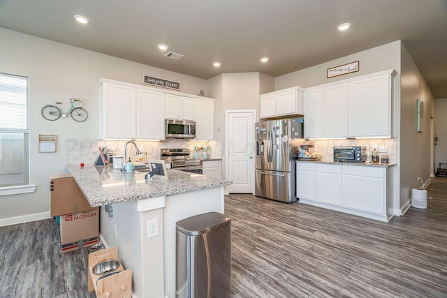 kitchen featuring stainless steel appliances, dark hardwood / wood-style flooring, kitchen peninsula, backsplash, and white cabinetry