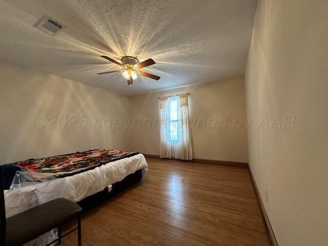 bedroom with baseboards, visible vents, wood finished floors, and a textured ceiling
