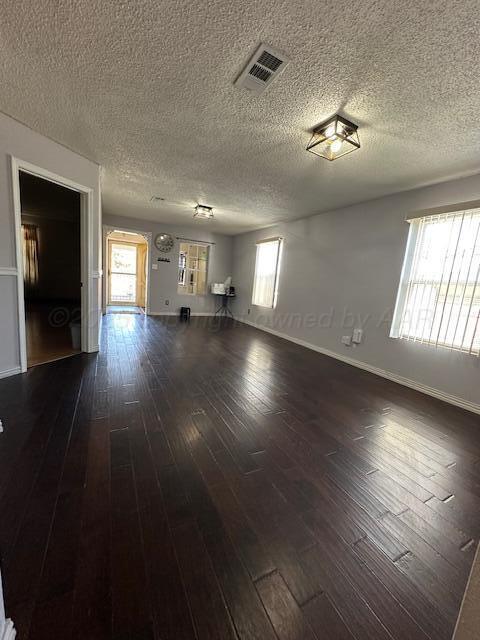unfurnished living room with a wealth of natural light, visible vents, dark wood-style floors, and baseboards