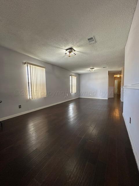 unfurnished room with a textured ceiling, dark wood-style flooring, and baseboards