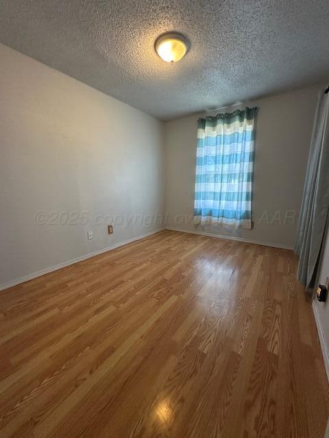 spare room featuring baseboards, wood finished floors, and a textured ceiling