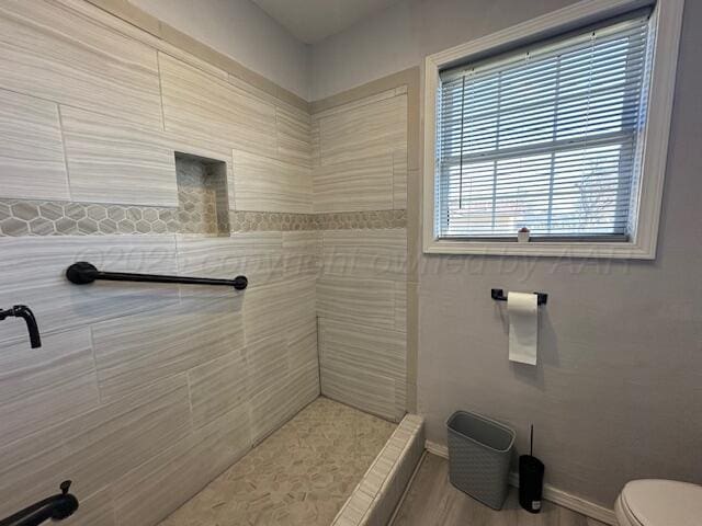 full bath featuring toilet, a tile shower, and baseboards
